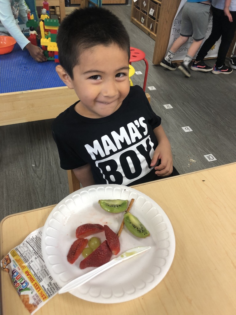 A little boy is showing off his flower he made with kiwi, strawberries, grapes, and pretzels.