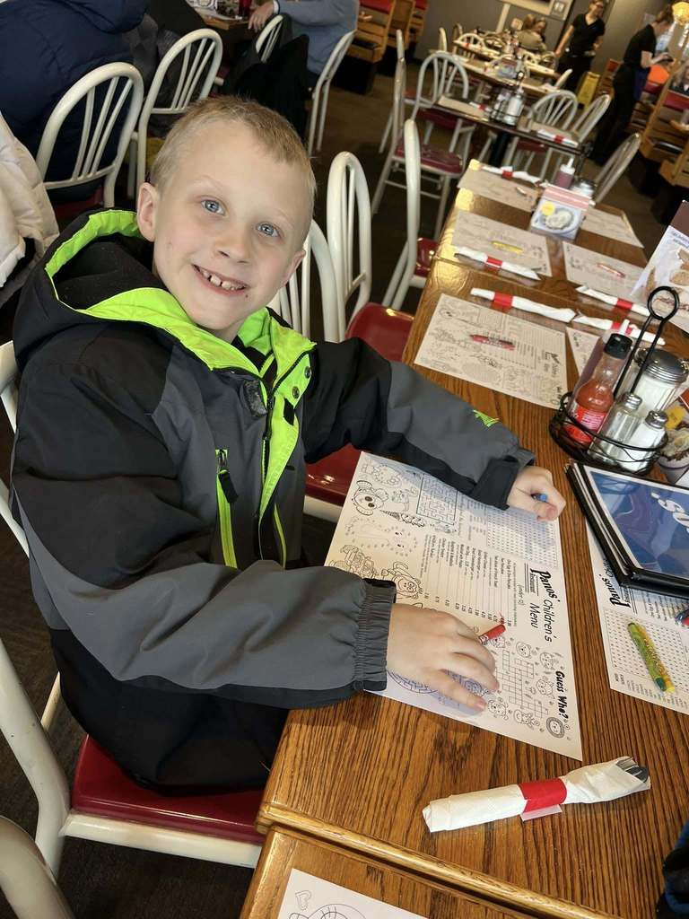 Young boy sitting inside a resteraunt with a menu in front of him smiling.