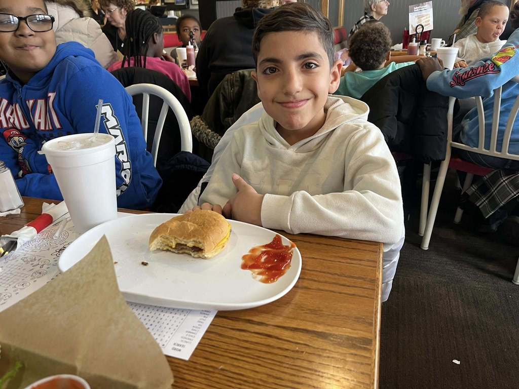 Young boy in a resteraunt with half an eaten sandwich in front of him.
