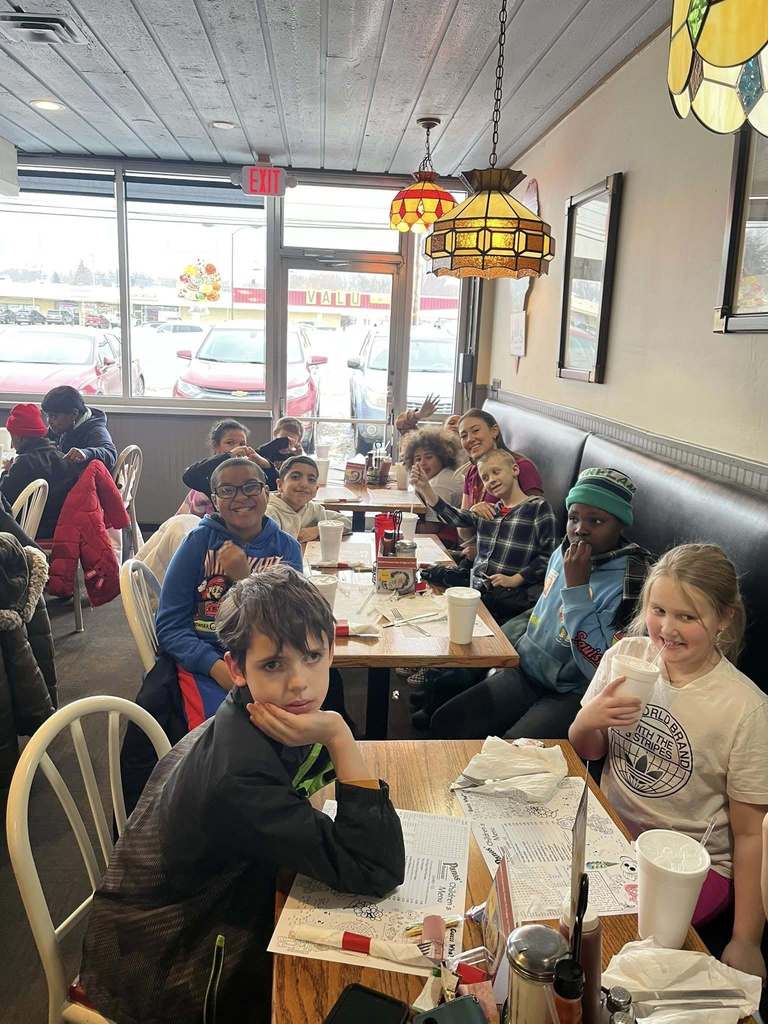 A group of kids sitting inside a restaurant and smiling.
