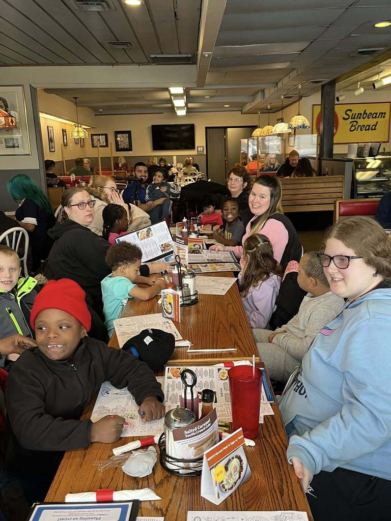 A group of kids and adults sitting inside a restaurant and smiling.