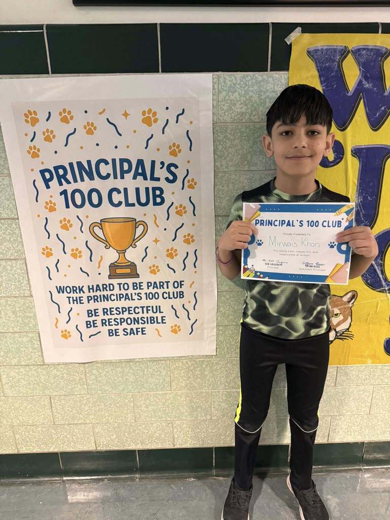 A young boy in a green and black shirt holding up his certificate.