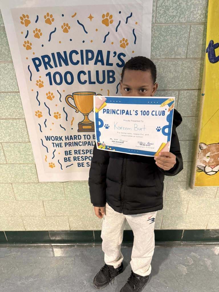 A young boy in a black jacket holding up his certificate.