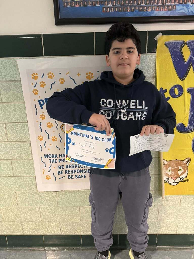 A young boy in a black hoodie holding up his certificate.