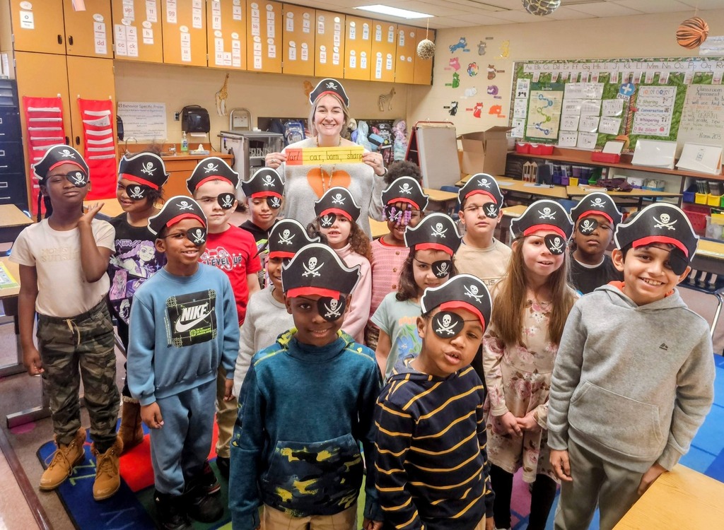 A group of students and one adult in a classroom wearing pirate hats and eyepatches.