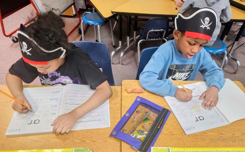 Kids writing in class with a pirate hat on his head.