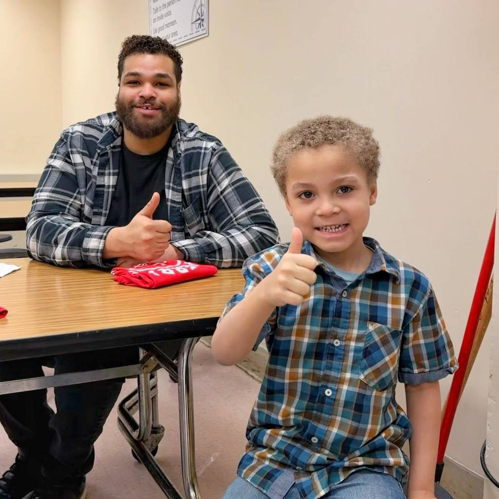 A young boy and man both wearing plaid shirts and holding a thumbs up. 