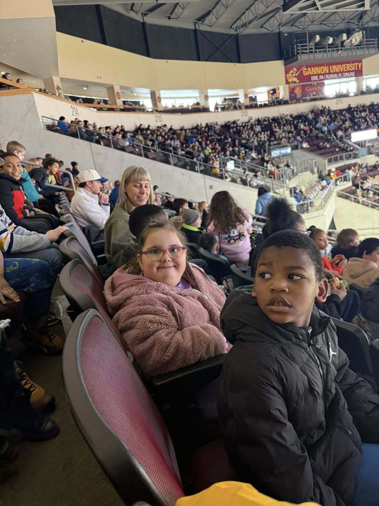 Kids and adults sitting in an arena.
