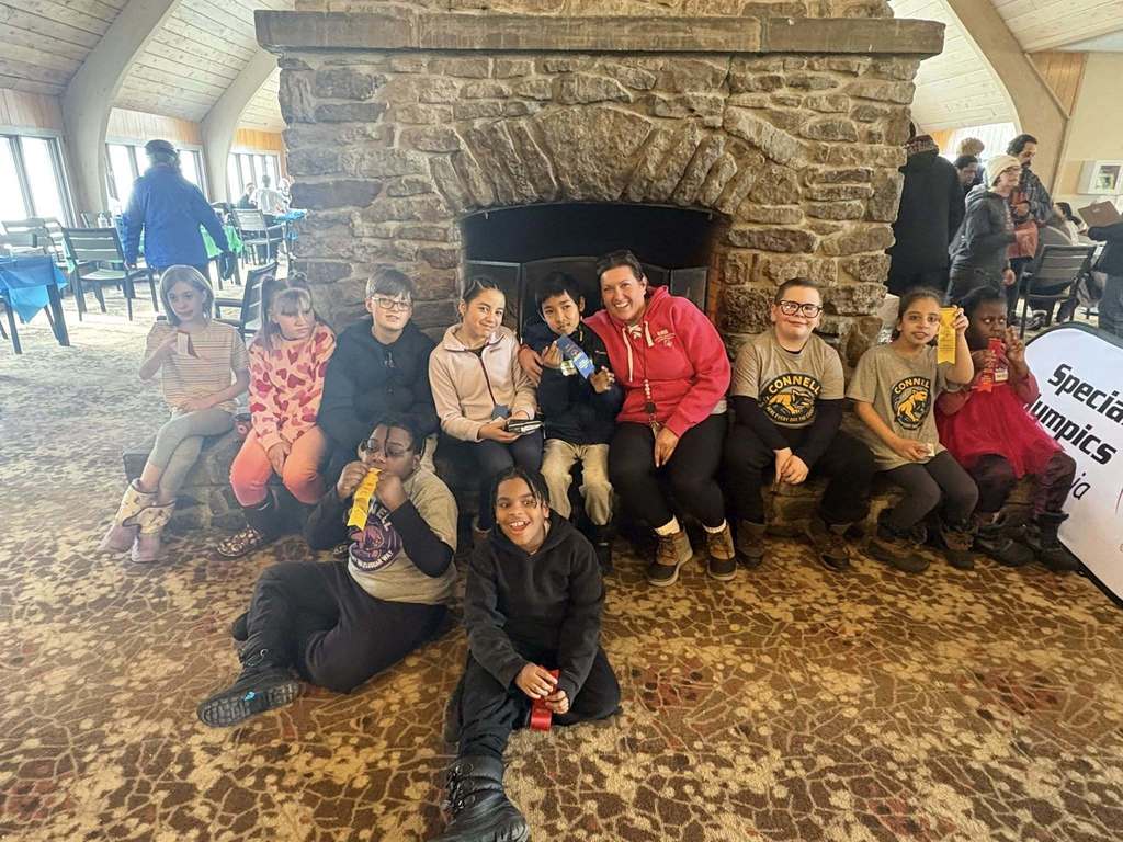 A group of kids and an adult in front of a fireplace smiling. 