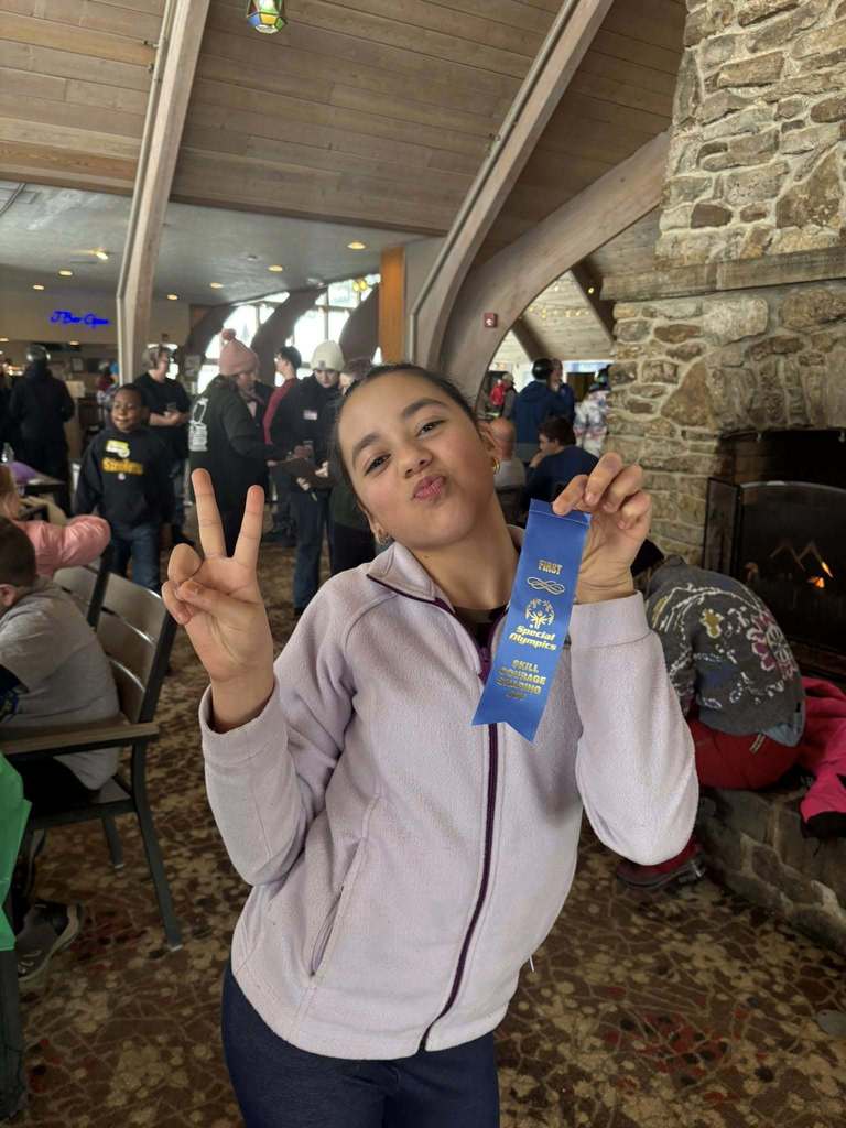 Young girl in a light purple jacket holding up two fingers up and her blue ribbon . 