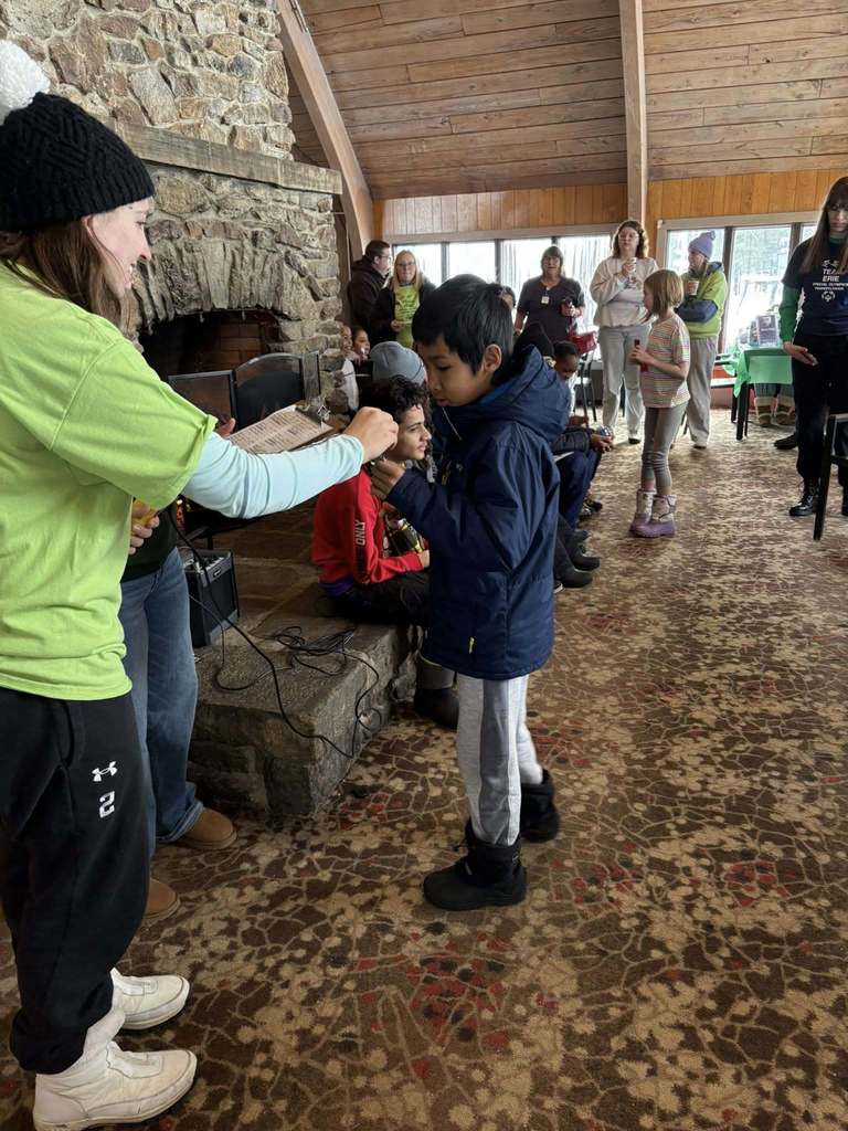 A women in a bright green shirt giving a ribbon to a boy in a navy blue jacket. 