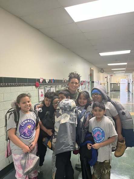 A group of kids and adult smiling in the hall of a school. 