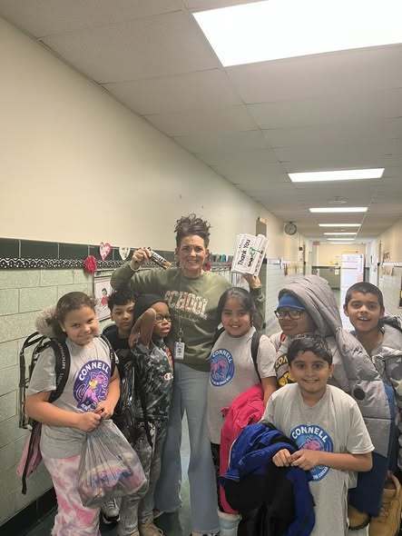 A group of kids and adult smiling in the hall of a school. 