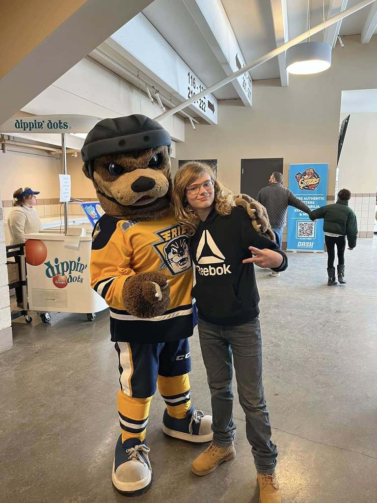 A kid standing next to an otter mascot. 