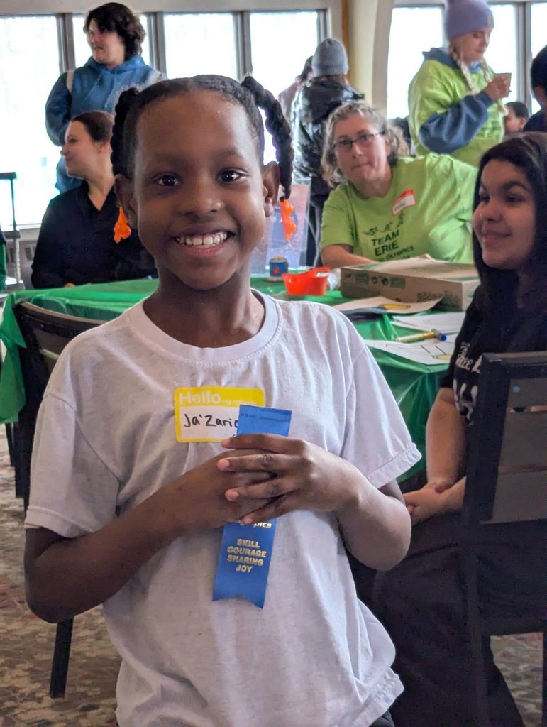 Young child wearing a gray shirt and holding up her blue ribbon. 