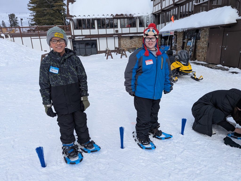 Kids smiling in the snow while wearing winter gear.
