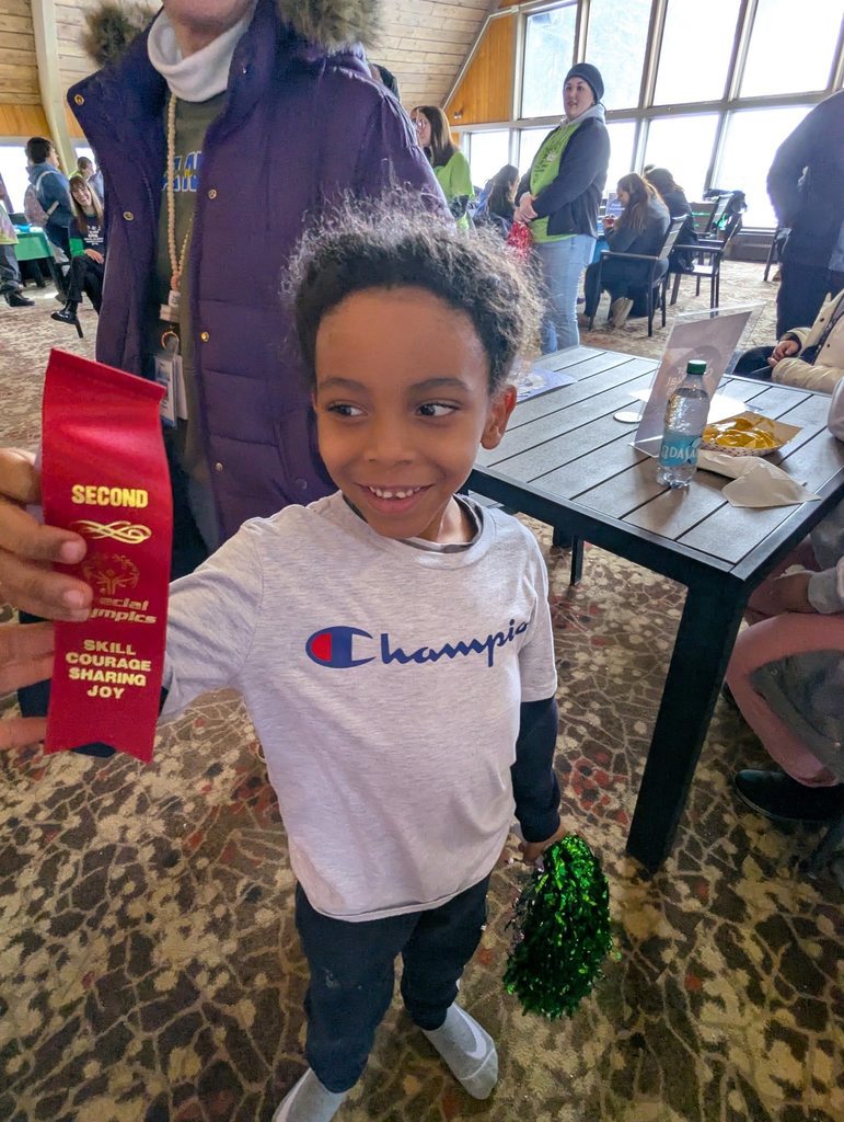 Young boy in a gray shirt holding up his red ribbon. 