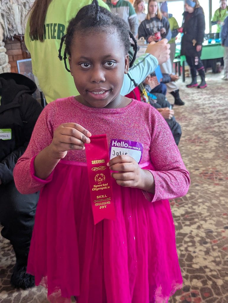Young girl in a pink top and holding a pink ribbon. 