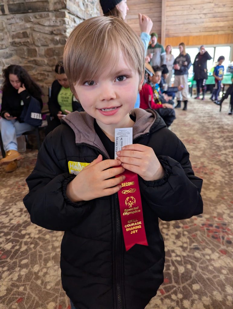 A young boy in a black jacket holding up his red ribbon. 