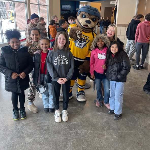 A group of kids smiling next to the Erie Otter's mascot. 