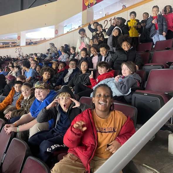 Kids sitting in an arena and smiling. 
