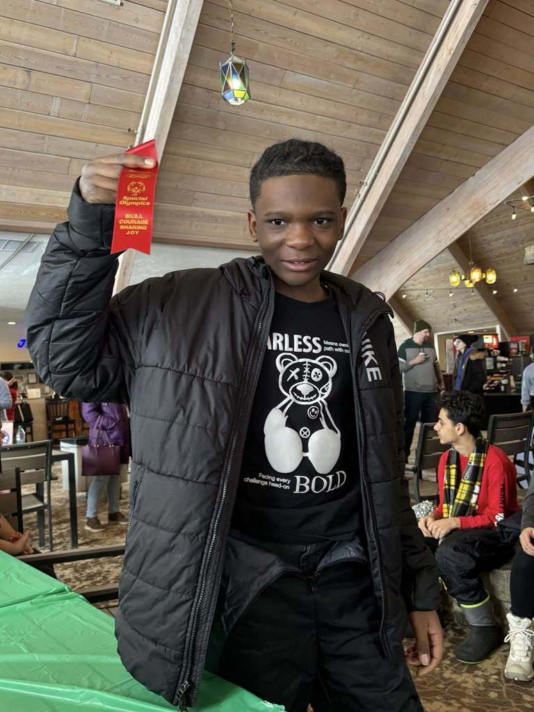 Young boy wearing a black jacket and holding up his red ribbon.