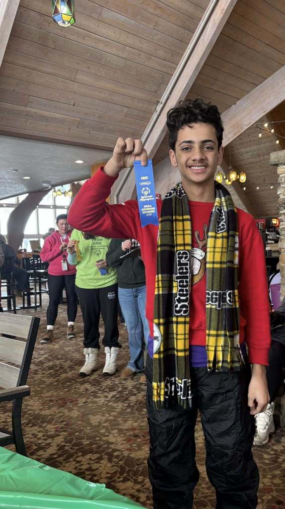 Young boy in a red shirt and Steelers scarf is holding up his blue ribbon. 