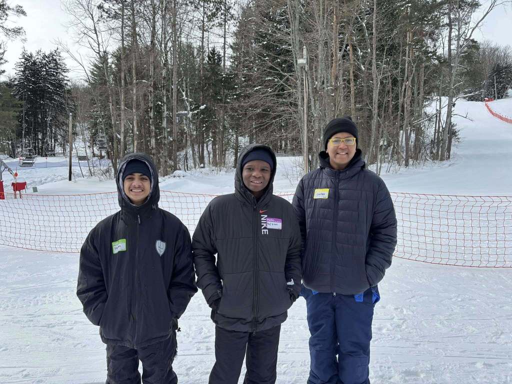 Three young boys in black jackets and hats smiling in the snow. 