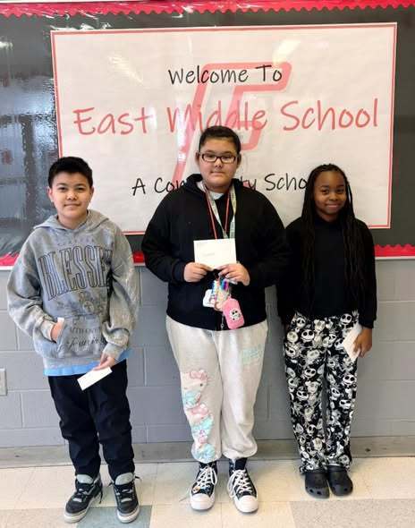 Thre students smiling in a hall.