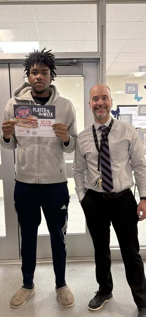 Young man wearing a light gray hoodie and holding up a paper while he stands next to a man with a striped tie.