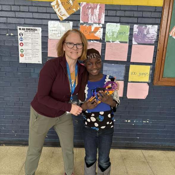 A young student standing with an adult and smiling. 