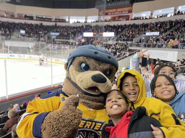Kids smiling next to the Erie Otters mascot. 