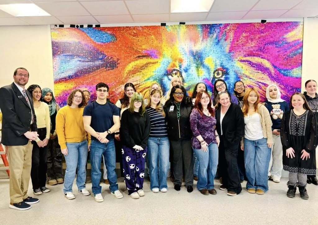 Students and adults standing in front of a colorful piece of art.