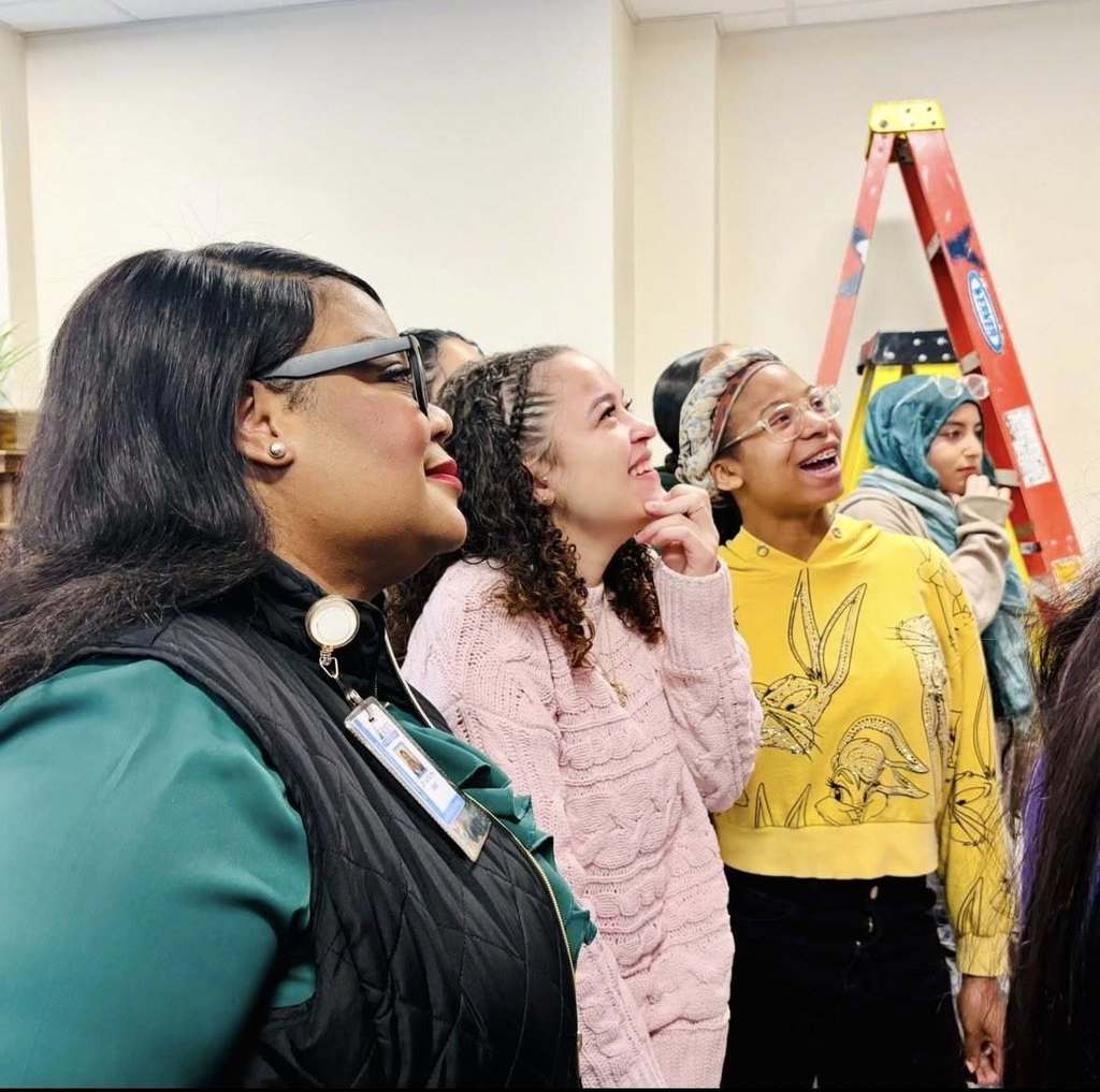 Students and adult admiring something on a wall.