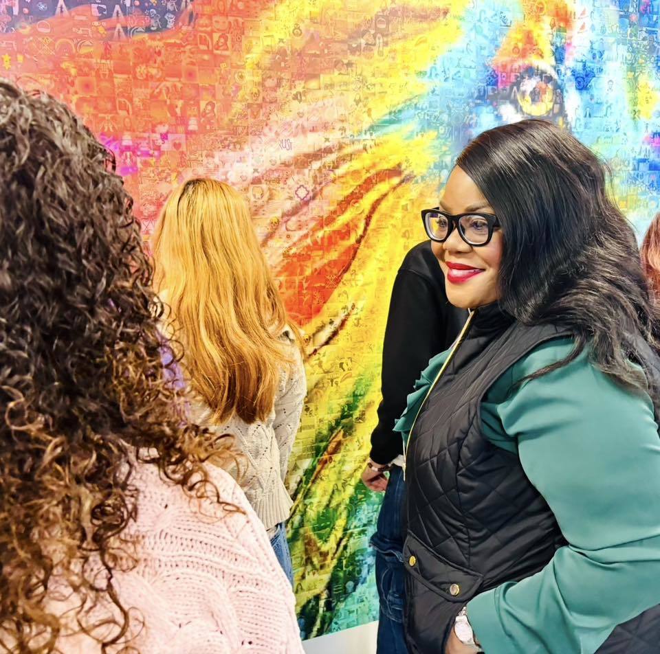 Women smiling in front of a colorful piece of art.