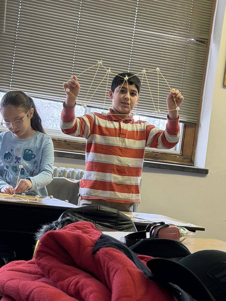 Student holding up his design he made from spaghetti and marshmallows. 