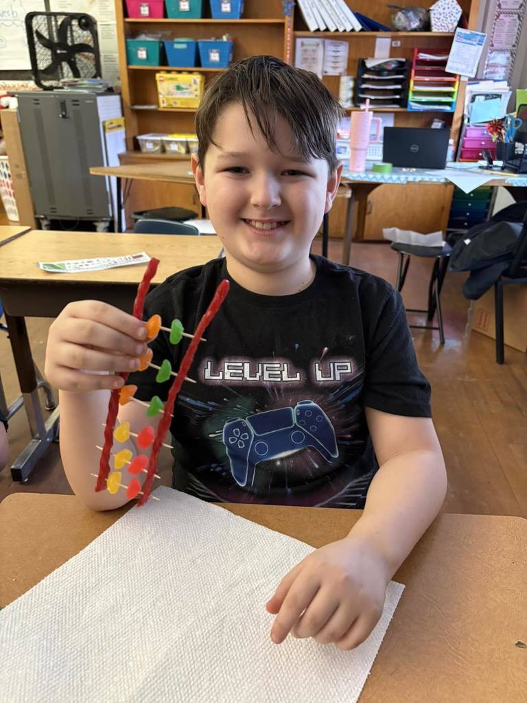 Young boy in a black shirt is putting candy on toothpick for a project. 