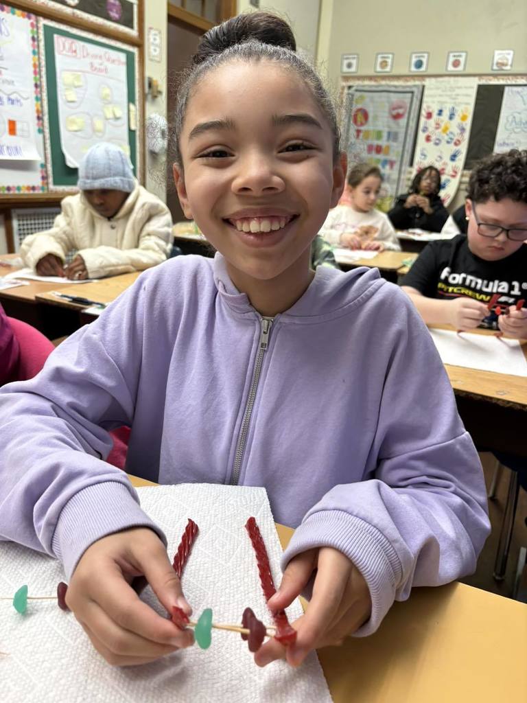 Young girl in a purple hoodie is putting candy on toothpick for a project. 