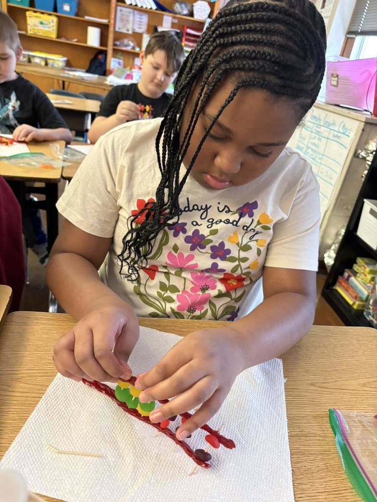 Young girl in a tan and floral shirt is putting candy on toothpick for a project. 