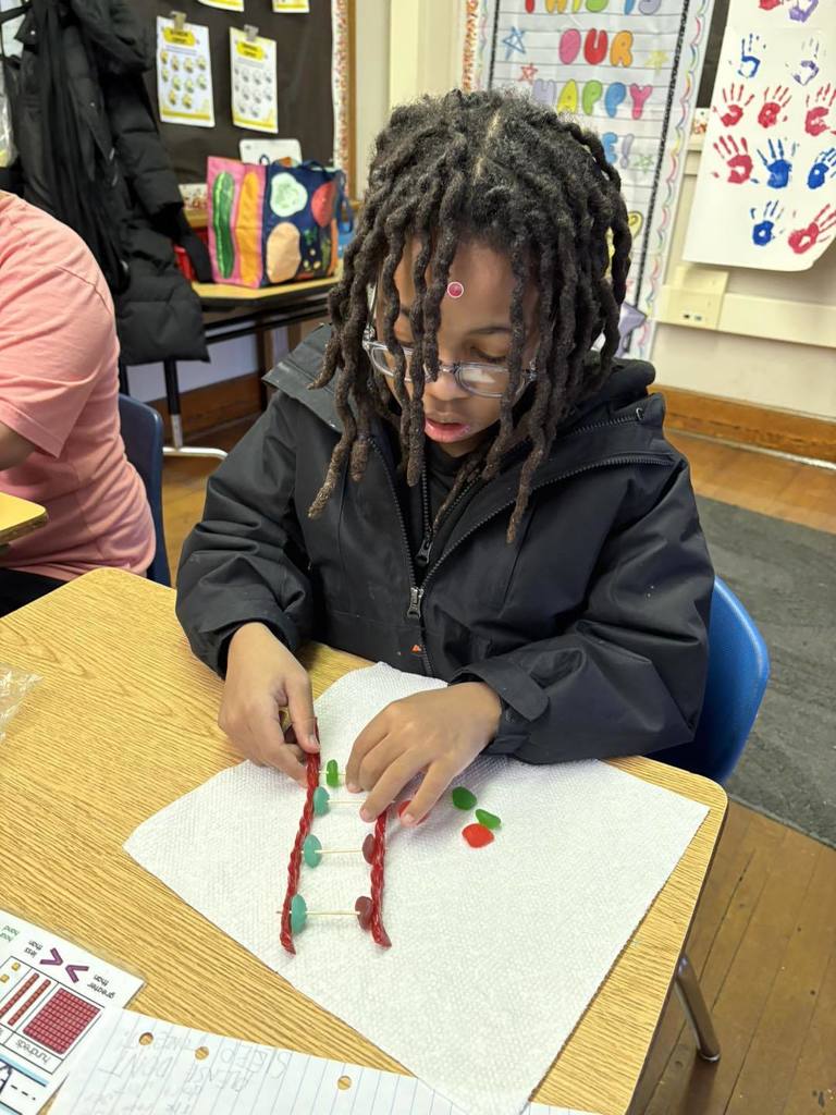 Kid in a black hoodie is putting candy on toothpick for a project. 