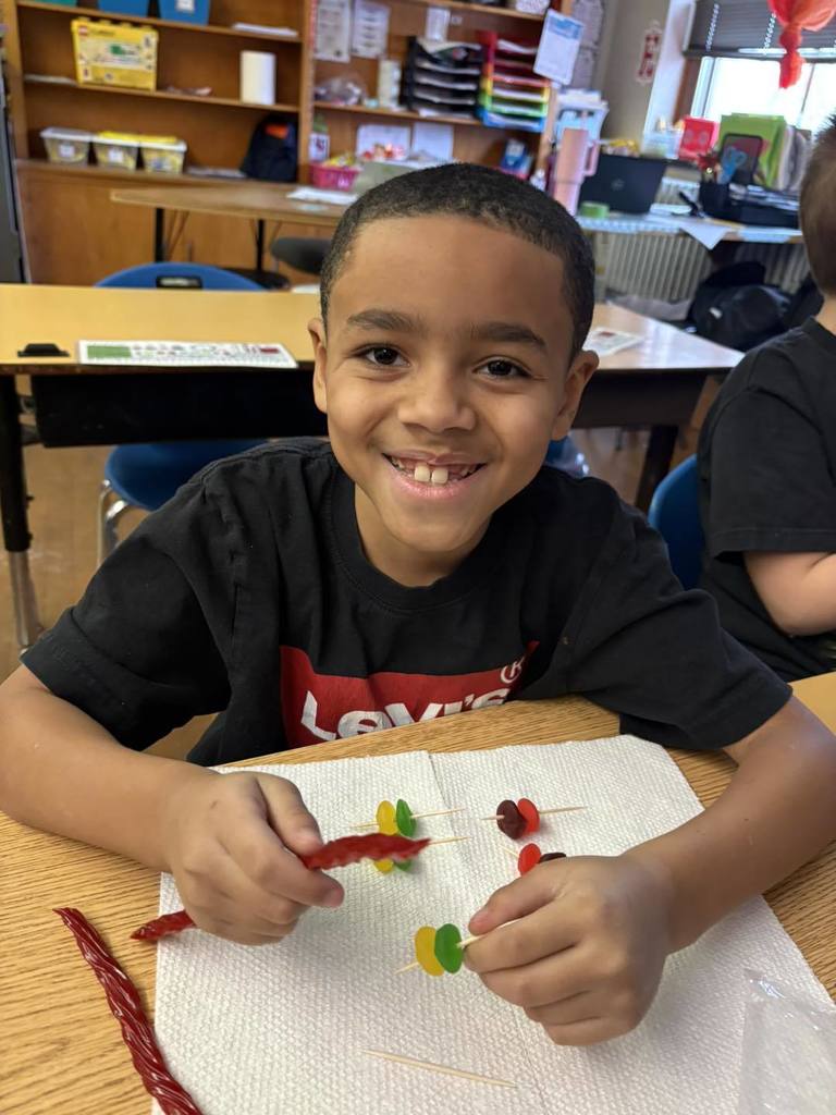 Young boy in a black shirt is putting candy on toothpick for a project. 