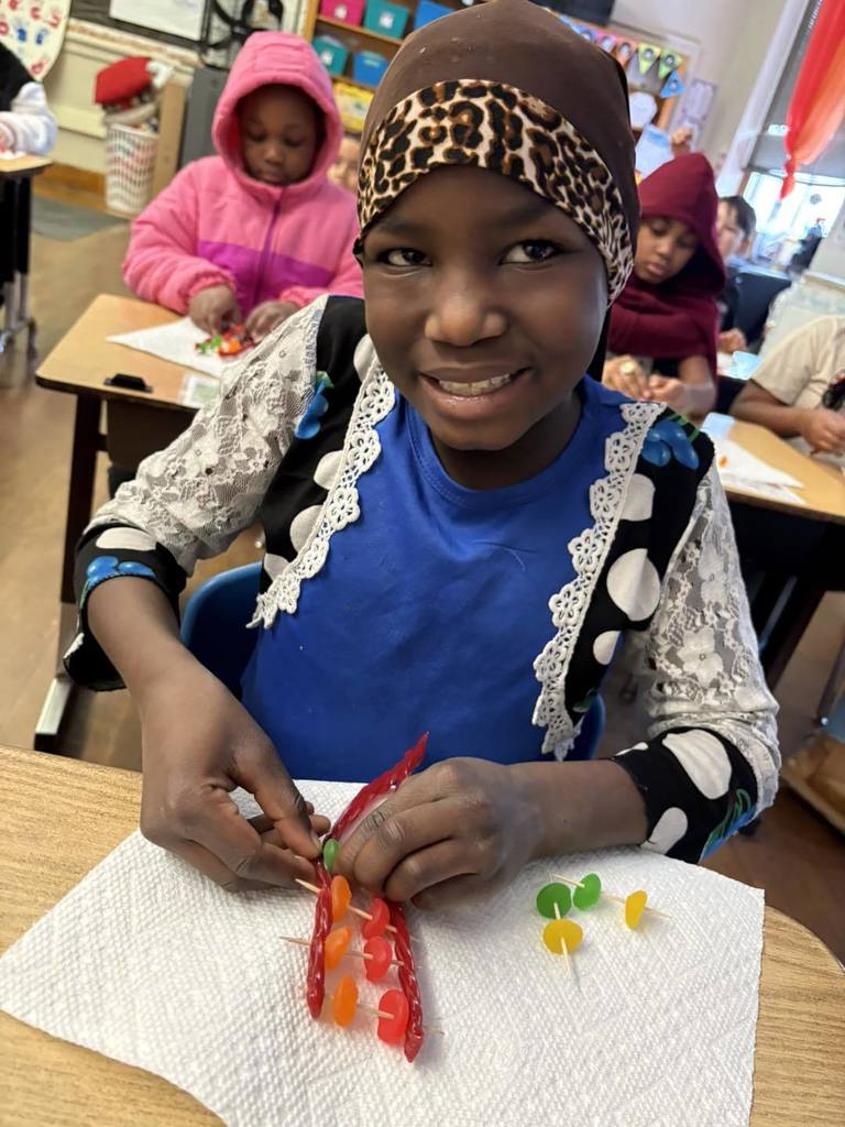 Young girl in a blue and white top is putting candy on toothpick for a project. 