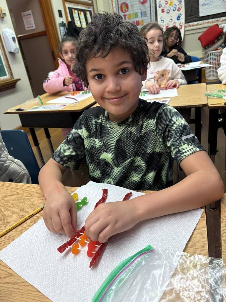 Young boy in a light and dark green shirt is putting candy on toothpick for a project. 