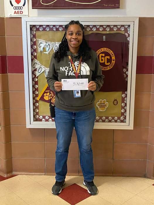 Young women in a gray hoodie holding an envelop in the hall and smiling.