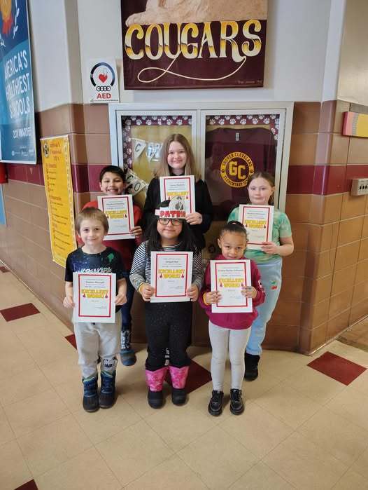 Students standing in a hall and holding up paper.