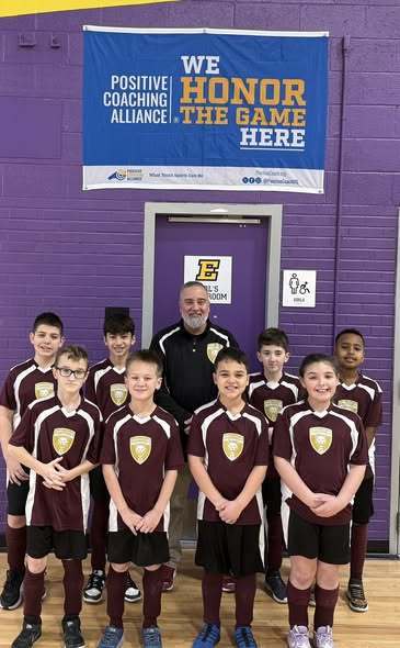 A group of young kids on a team smiling with their coach.