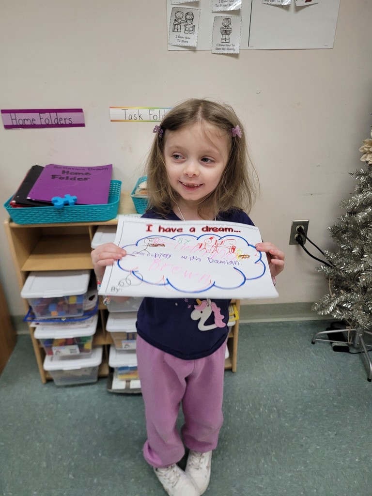 Young girl wearing pink pants is holding her paper up that she colored.