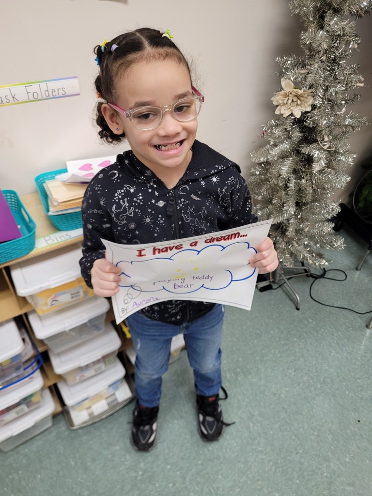 Young girl in a black hoodie with silver designs is holding her paper up that she colored.
