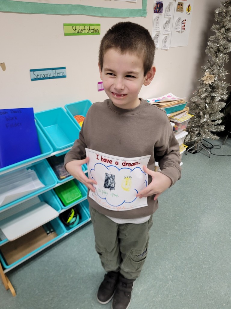 Young boy wearing a brown shirt is holding her paper up that he colored.