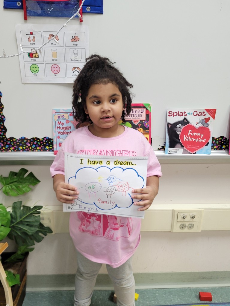 Young girl wearing a pink shirt is holding her paper up that she colored.